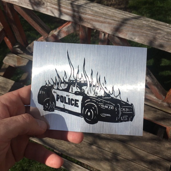 shiny chrome sticker that looks like brushed metal with a black print of a burning police car